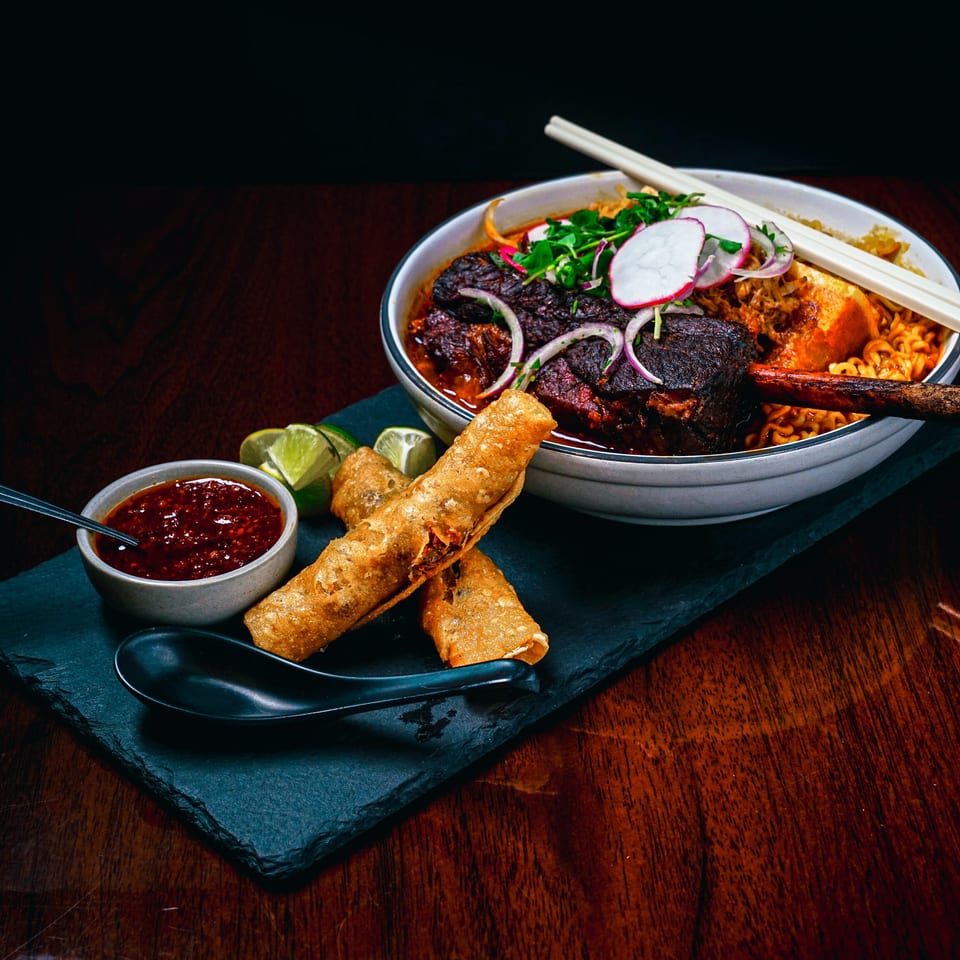Braised short rib ramen with radishes, onions, and cilantro, served with crispy spring rolls and chili sauce.