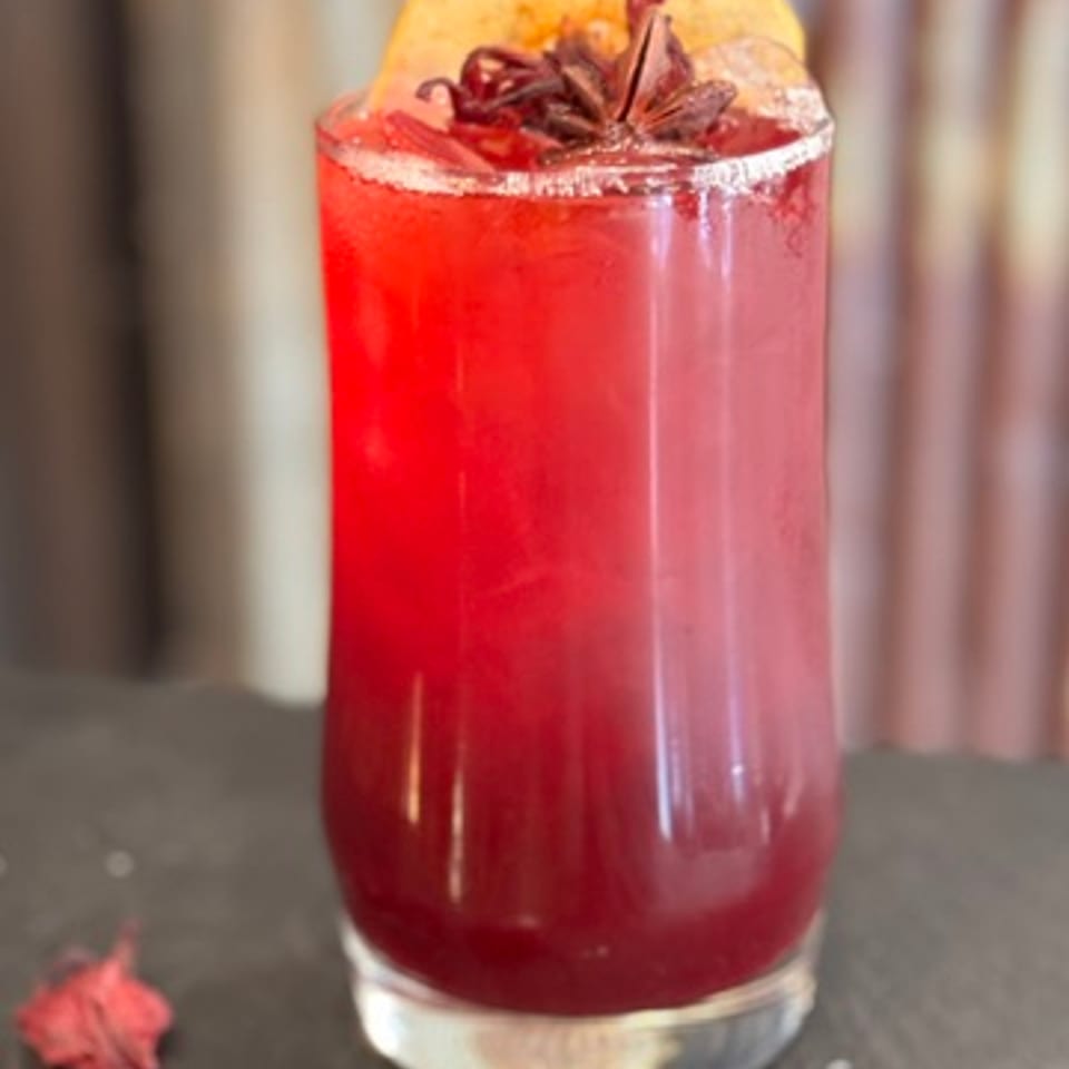 Vibrant red drink with a fruit slice and star anise garnish on a dark slate.
